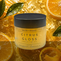 Jar of 'Citrus Gloss' by milk+moss with oranges and leaves in the background