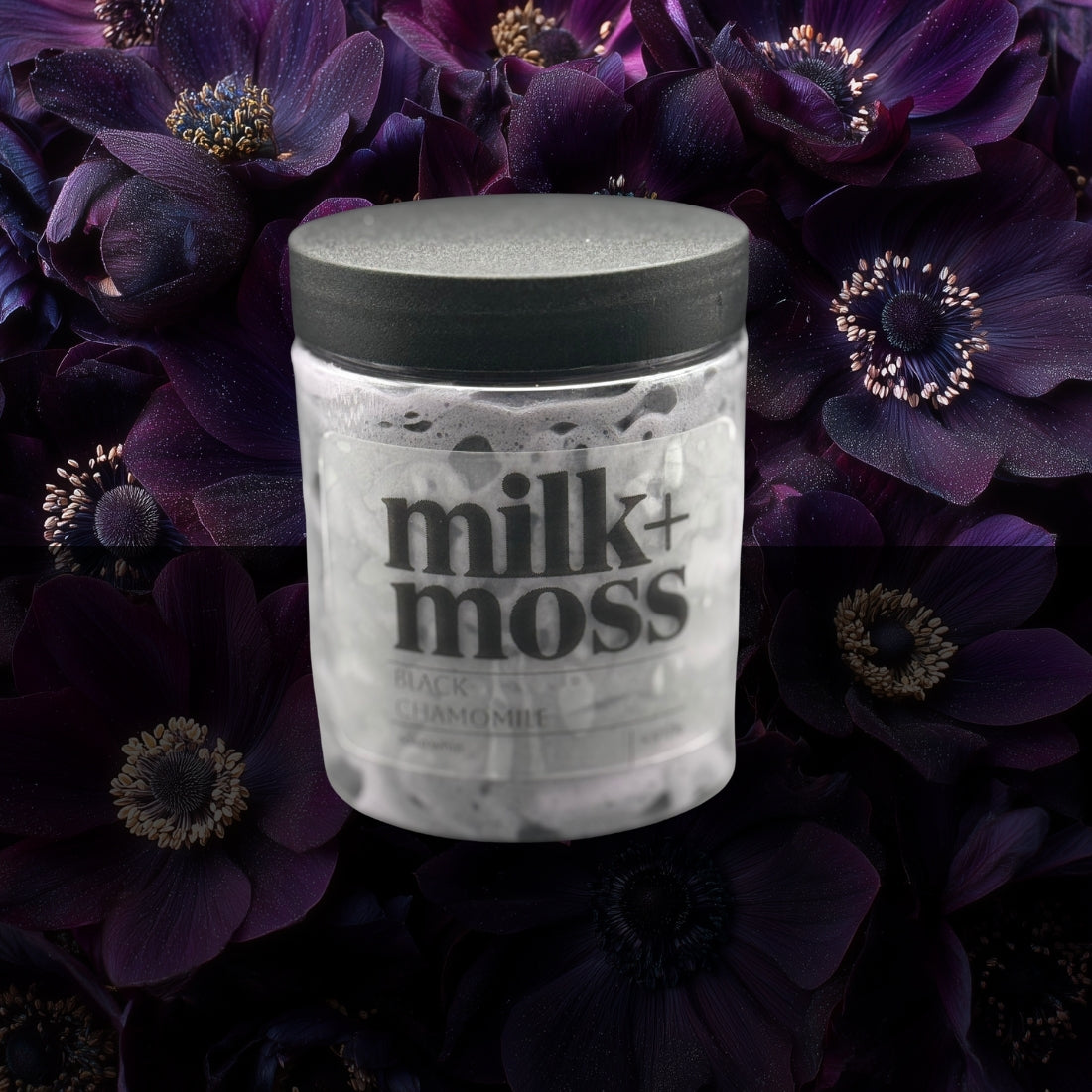 Jar of 'milk+moss' product surrounded by dark purple flowers