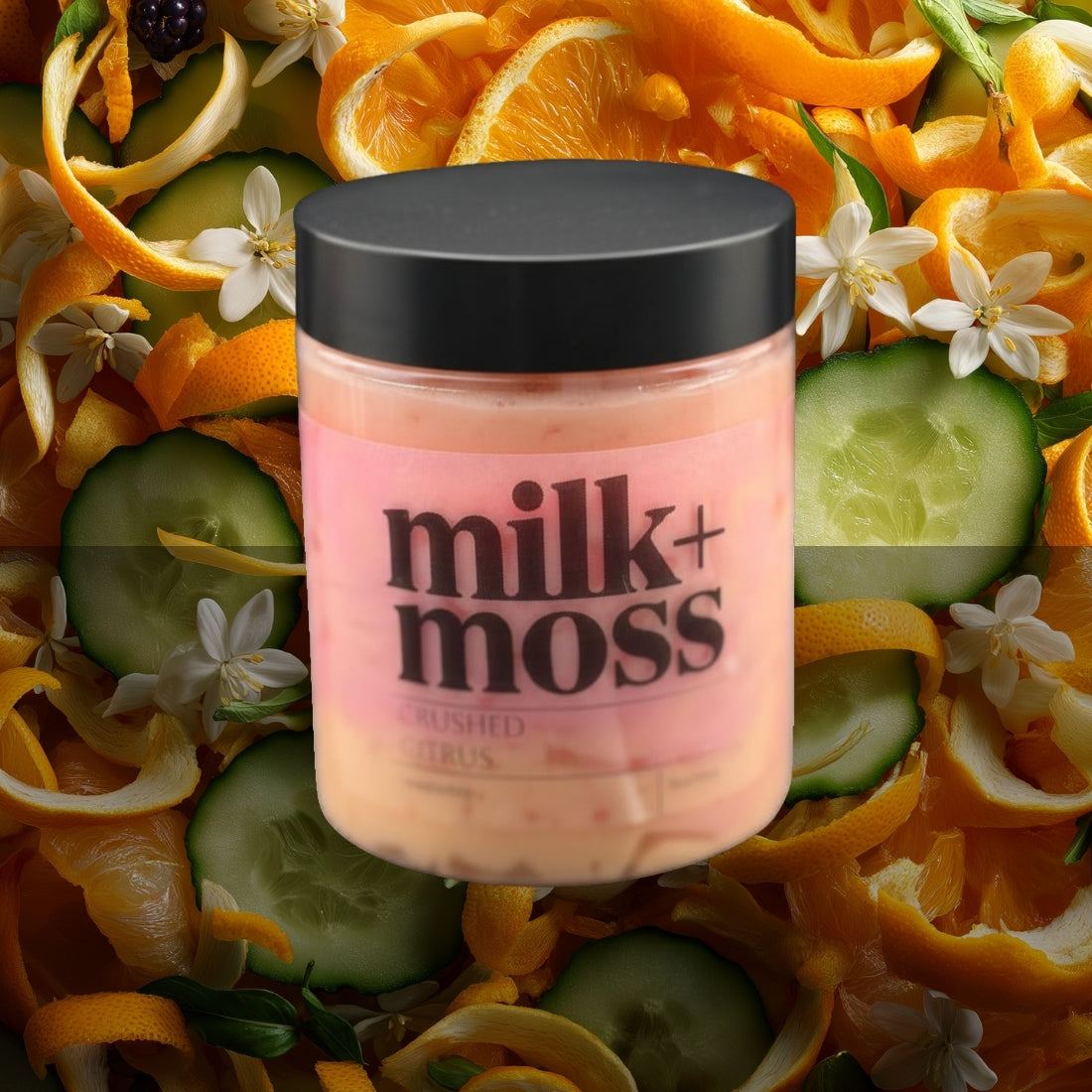 Jar of 'milk+moss' product surrounded by orange peels, cucumbers, and flowers.