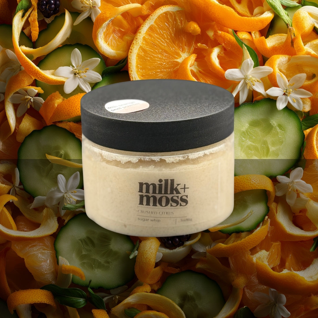 Jar of milk+moss product surrounded by orange peels, cucumbers, and flowers